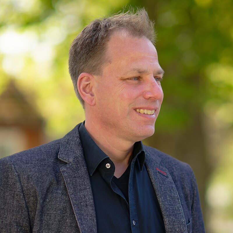 Foto von Markus Irion in dunklem Shirt und Jackett vor einem verschwommenen grünen Naturhintergrund. Der Diplom-Pädagoge beschäftigt sich seit vielen Jahren mit der Unterstützung von Menschen im Autismus-Spektrum.