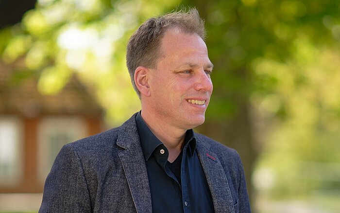 Foto von Markus Irion in dunklem Shirt und Jackett vor einem verschwommenen grünen Naturhintergrund. Der Diplom-Pädagoge beschäftigt sich seit vielen Jahren mit der Unterstützung von Menschen im Autismus-Spektrum. 