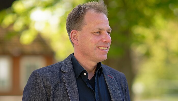 Foto von Markus Irion in dunklem Shirt und Jackett vor einem verschwommenen grünen Naturhintergrund. Der Diplom-Pädagoge beschäftigt sich seit vielen Jahren mit der Unterstützung von Menschen im Autismus-Spektrum.