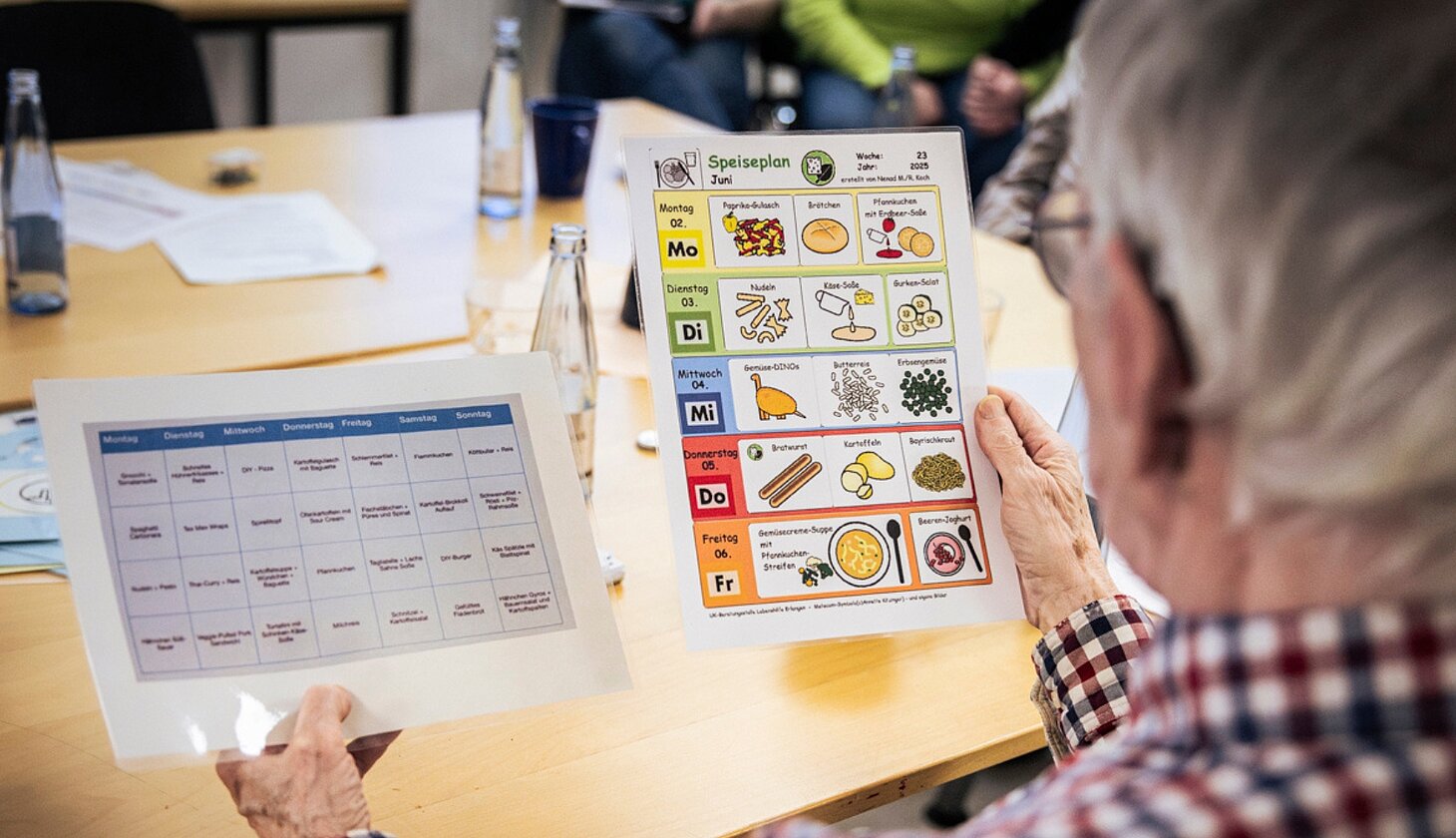 Eine Person vergleicht zwei Versionen eines Essensplans: einen mit Text und einen mit Symbolen, die das Essen darstellen.