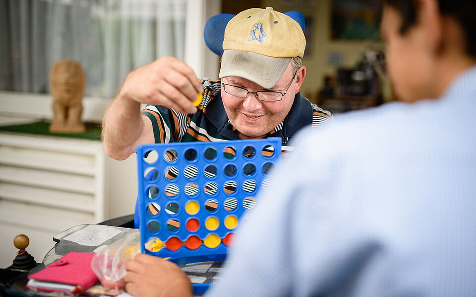 Mann im Rollstuhl spielt 4 gewinnt mit Mitarbeiter