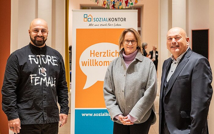 Der EU-Jugendbotschafter Ali Mahlodji steht lächelnd mit zwei weiteren Personen vor einem Banner mit der Aufschrift