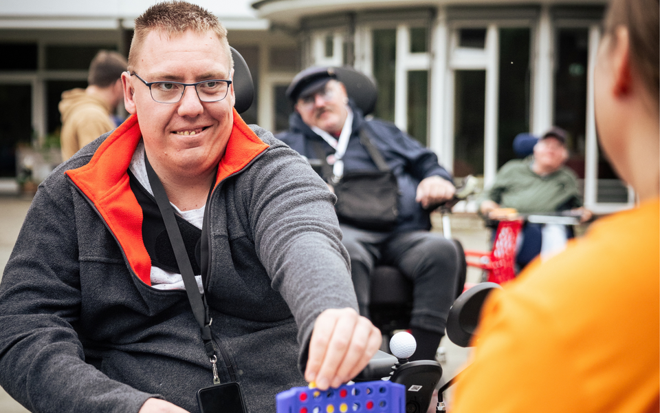 Ein Mann im Rollstuhl spielt mit einer weiteren Person Vier gewinnt im Außenbereich des Senator-Neumann-Hauses des Sozialkontors.