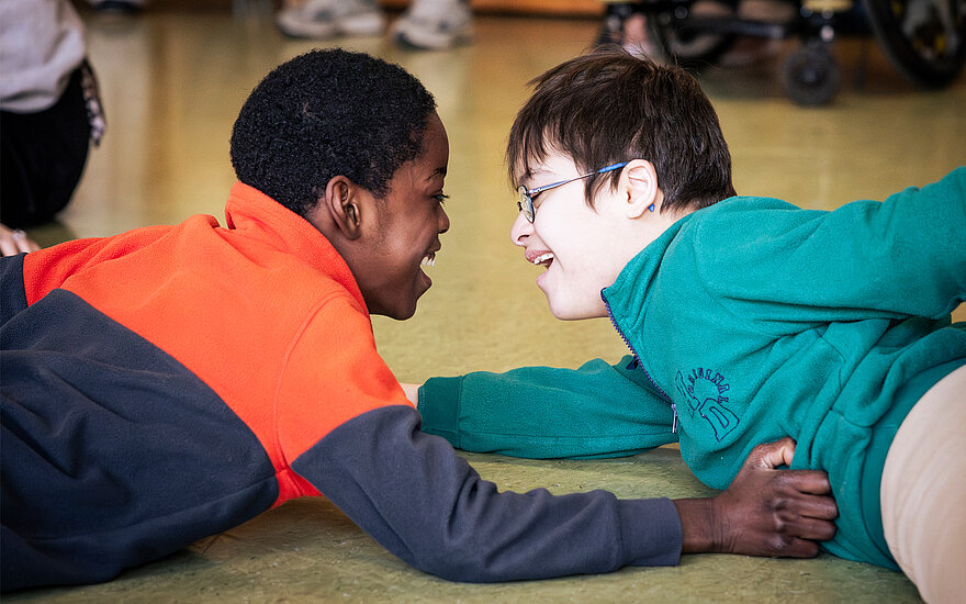 Zwei Jungen liegen auf dem Boden und lächeln sich an.