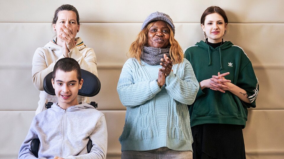Ein Jugendlicher im Rollstuhl sitzt vor drei Menschen, die applaudieren und lächeln. Die Gruppe begleitet das Hip-Hop-Projekt in der Ferienbetreuung des Sozialkontors.