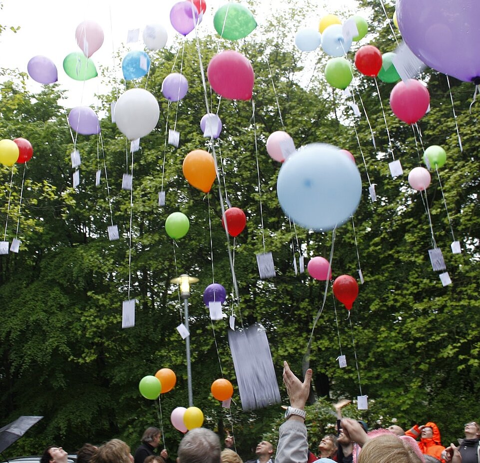 Viele bunte Luftballons steigen in den Himmel, jeder Luftballon hat eine Karte an seinem Bändchen hängen.