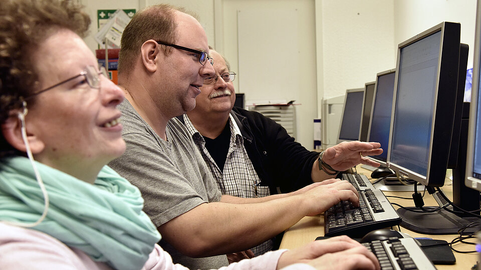 Drei Personen sitzen vor Computer-Bildschirmen
