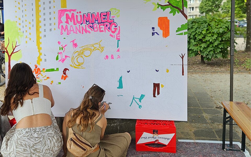 Zwei Teilnehmende gestalten im Freien eine große Bildfläche mit dem Schriftzug „Mümmelmannsberg“ und Motiven aus dem Stadtteil.