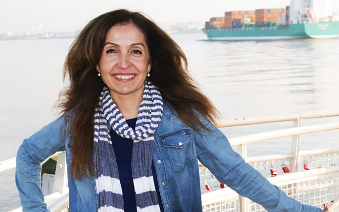 Filiz Demirel, eine Politikerin der Partei Bündnis 90/Die Grünen Hamburg, steht am Hamburger Hafen und lächelt in die Kamera.