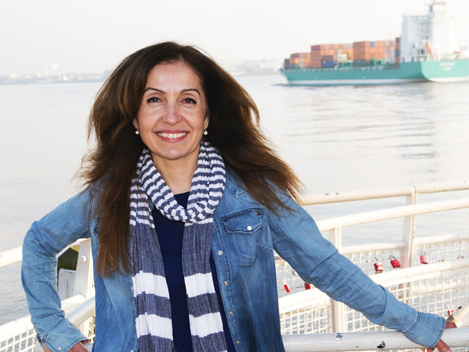 Filiz Demirel, eine Politikerin der Partei Bündnis 90/Die Grünen Hamburg, steht am Hamburger Hafen und lächelt in die Kamera.