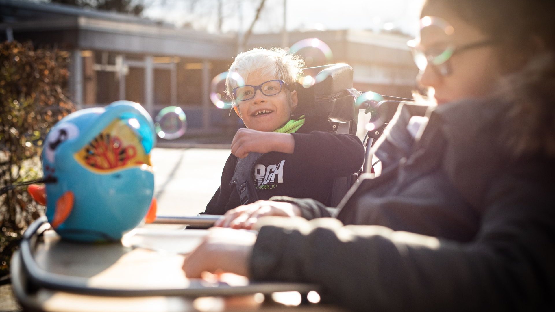 Ein Förderschüler und eine Förderschülerin im Rollstuhl spielt draußen mit Seifenblasen.