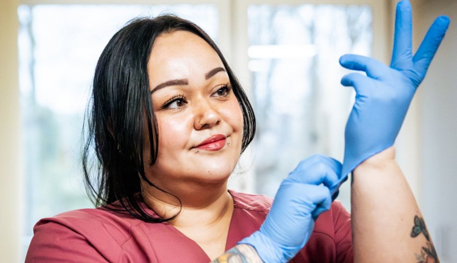 Eine Frau in roter medizinischer Kleidung zieht sich einen Gummihandschuh über.