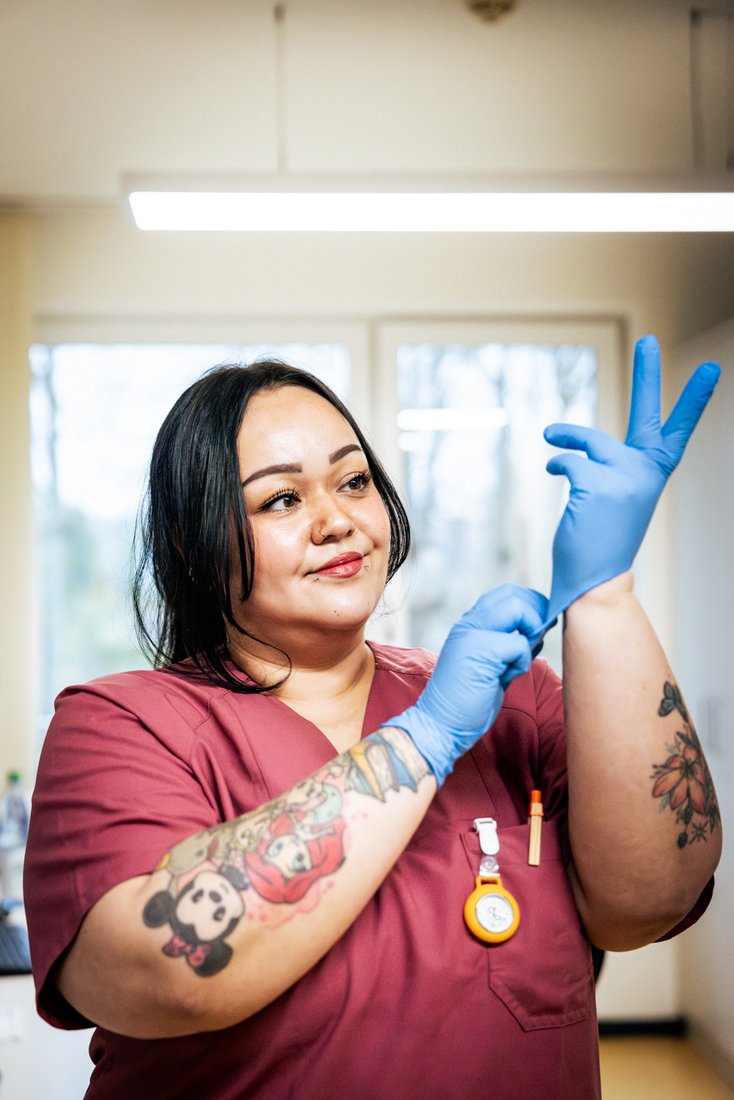 Eine Frau in roter medizinischer Kleidung zieht sich einen Gummihandschuh über.