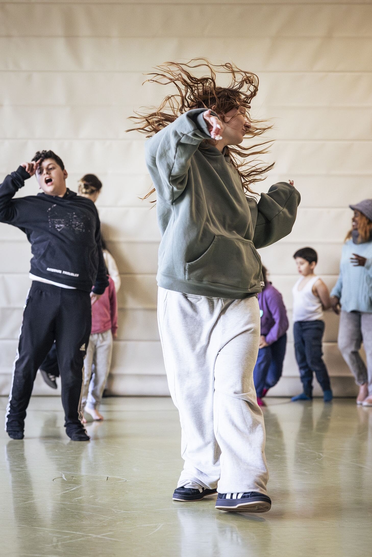 Eine Jugendliche mit langen, wehenden Haaren tanzt mit kraftvoller Bewegung in der Mitte der Turnhalle. Ihr Gesichtsausdruck ist konzentriert und im Hintergrund folgen weitere Kinder ihrer Choreographie.