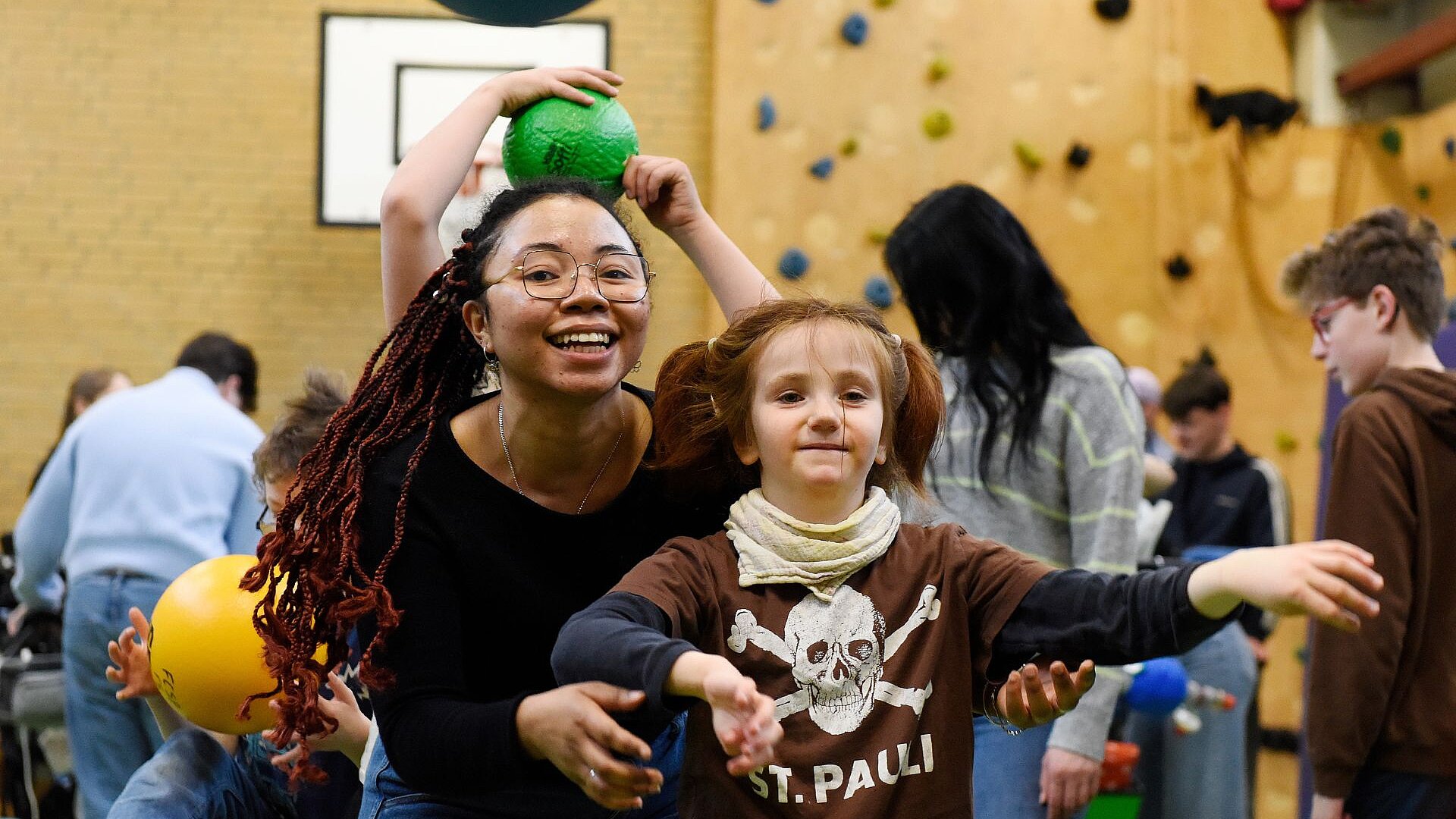 Mitarbeiterin lacht mit einer Förderschülerin beim Ballspiel in der Sporthalle.