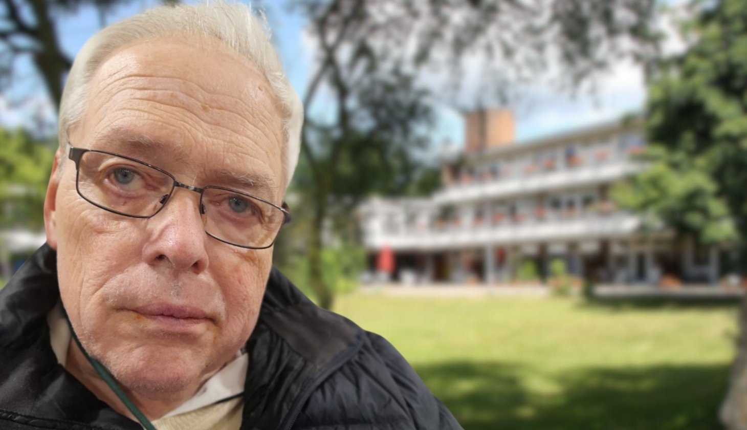 Roland Tessner im Vordergrund, mit Brille und freundlichem Blick. Im Hintergrund das Senator-Neumann-Haus, umgeben von einer grünen Wiese und Bäumen.