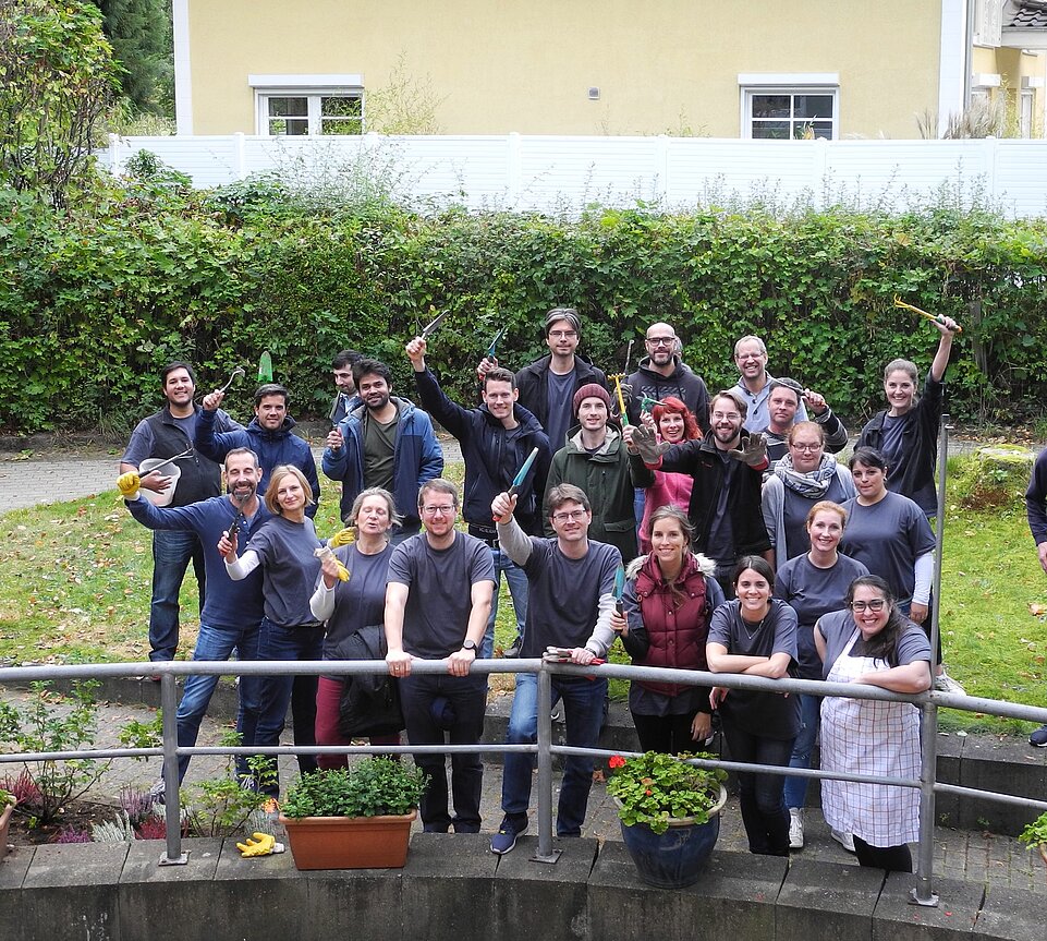 Eine Gruppe von Menschen gucken in die Kamera, jeder hat ein Gartenwerkzeug in der Hand oder eine Schürze um