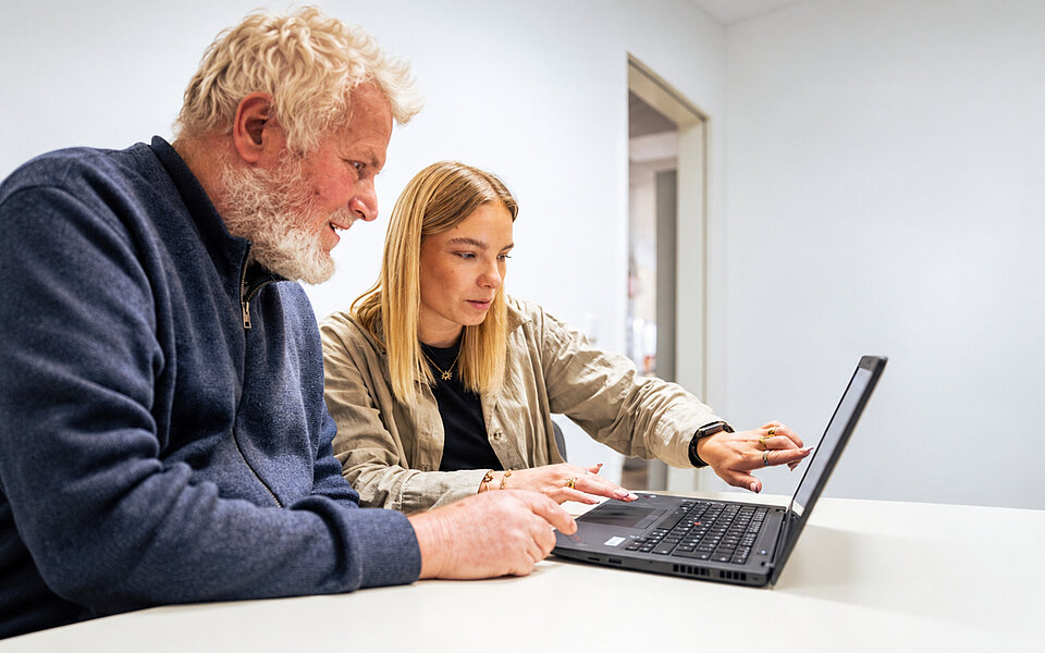Assistenz im Alltag beim Sozialkontor: Ein älterer Mann und eine junge Frau nutzen gemeinsam einen Laptop.