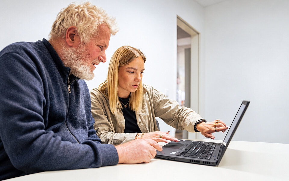 Assistenz im Alltag beim Sozialkontor: Ein älterer Mann und eine junge Frau nutzen gemeinsam einen Laptop.