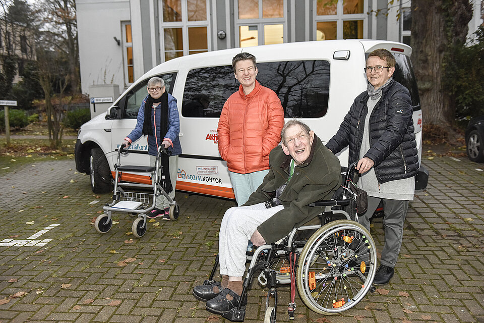 Vier Personen, davon eine im Rollstuhl vor einem Auto stehend