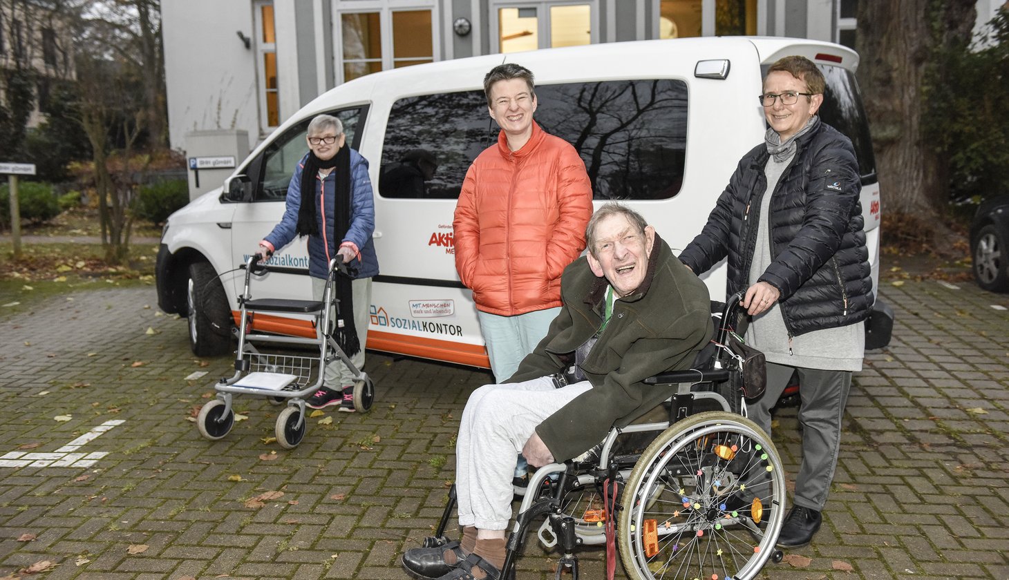 Vier Personen, davon eine im Rollstuhl vor einem Auto stehend