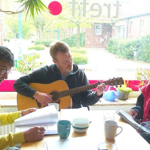 Drei Männer musizieren, an einem Tisch sitzend