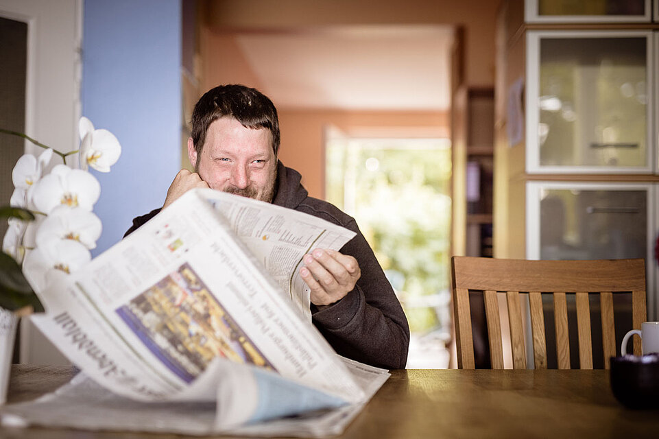 In einem Raum. Mann sitzt an einem Tisch mit einer Zeitung.