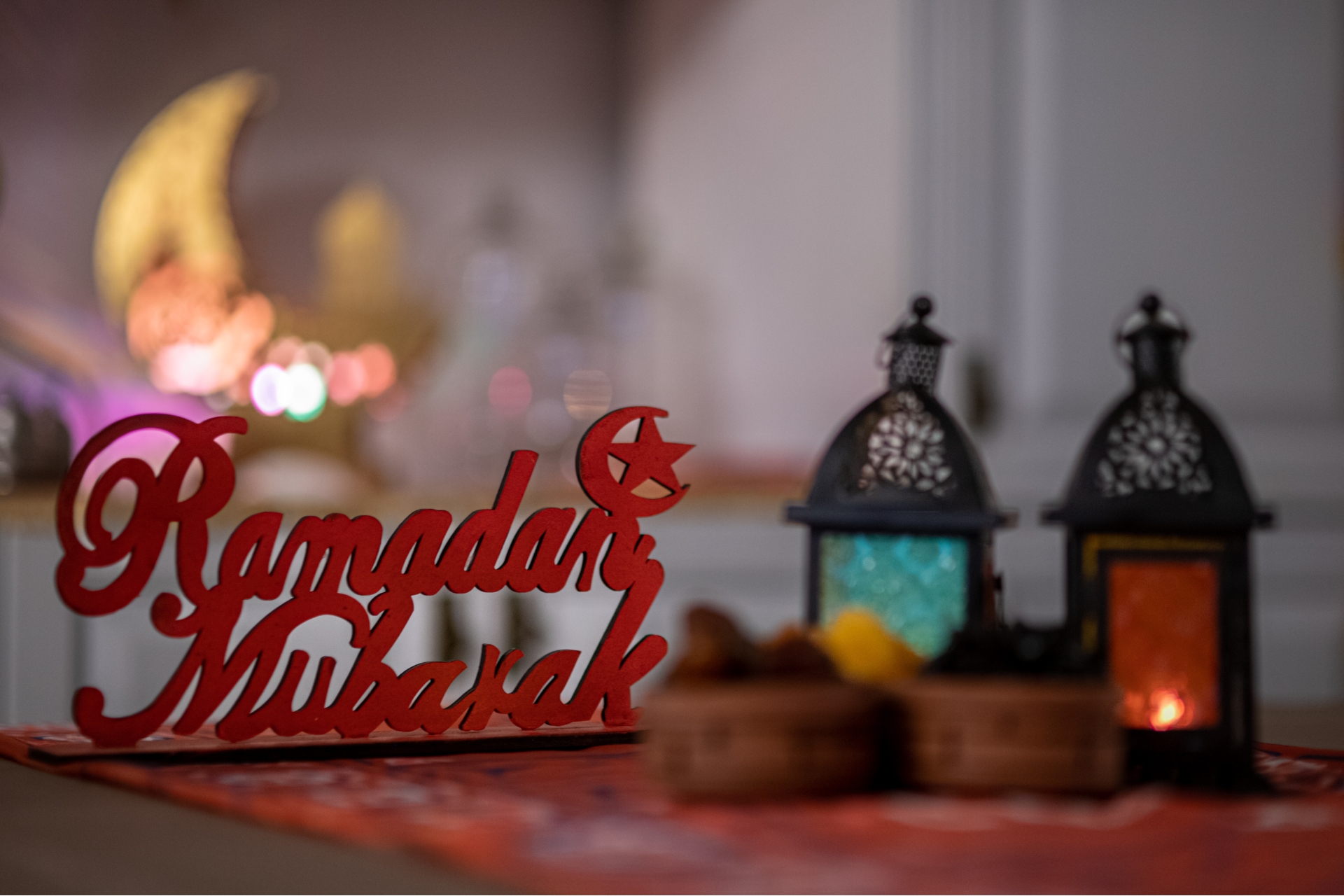 Dekoratives Arrangement mit zwei orientalischen Laternen und einem Schriftzug aus Holz, der „Ramadan Mubarak“ zeigt. Im Hintergrund leuchten unscharfe Lichter in warmen Farben.